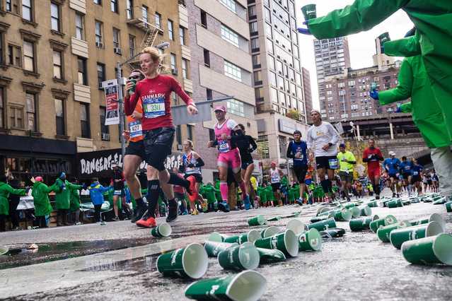 Runners at Boston marathon running through water station with focus on green paper cups on ground